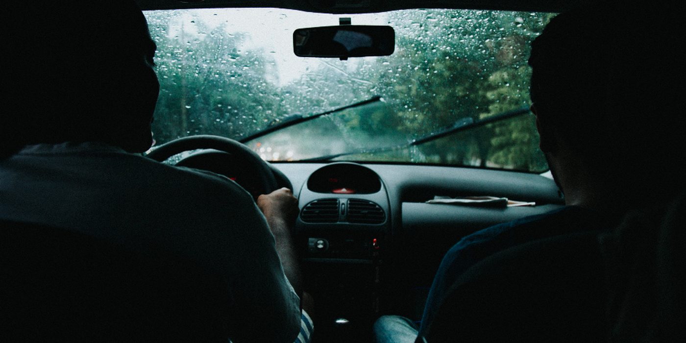 The view from inside a car through a rain-covered windscreen onto a wet road.