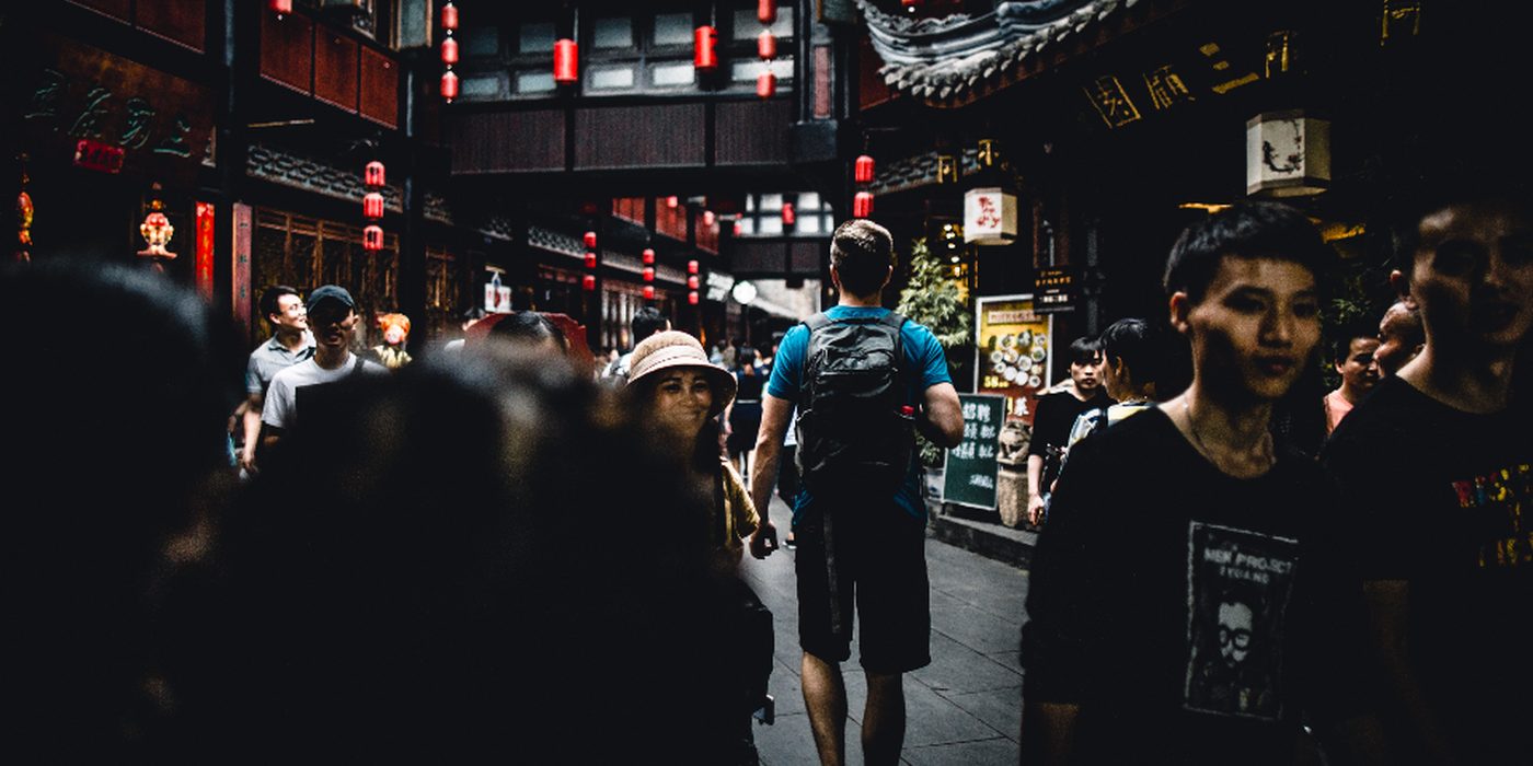 A traveller with a backpack walking through a busy covered market street.