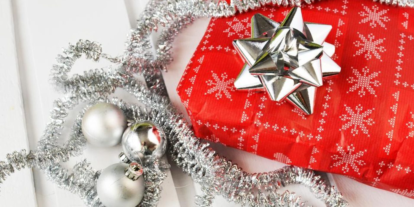 A red gift box finished with a silver bow, surrounded by baubles and tinsel.