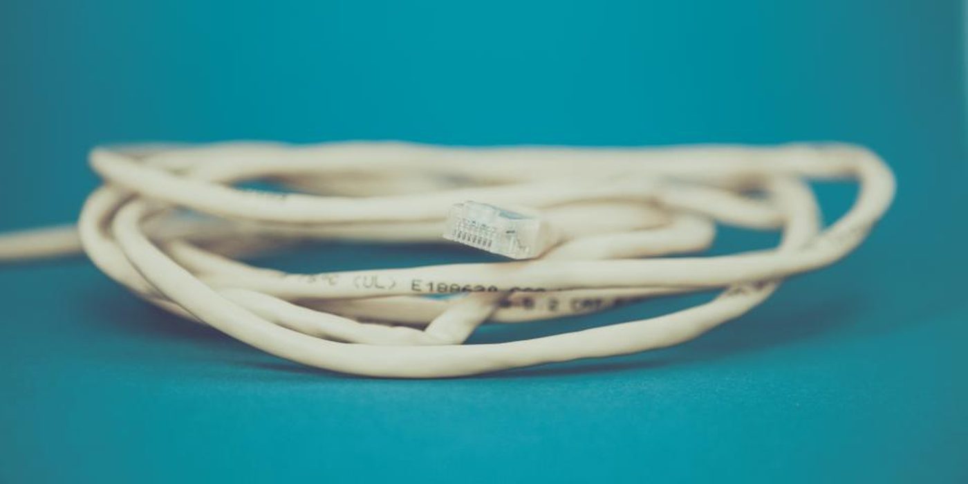 A white network cable coiled neatly on a plain teal background.