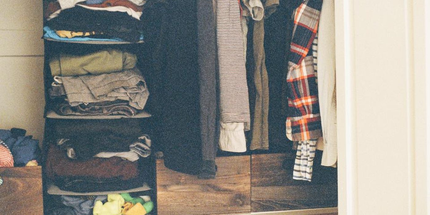 A hanging fabric closet organiser holding folded shirts and jeans, next to coats on a rail.