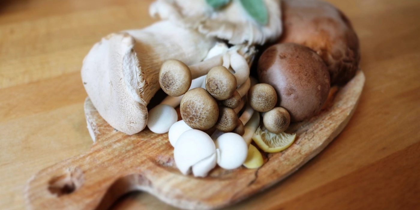 Assorted button and chestnut mushrooms on a round wooden chopping board.