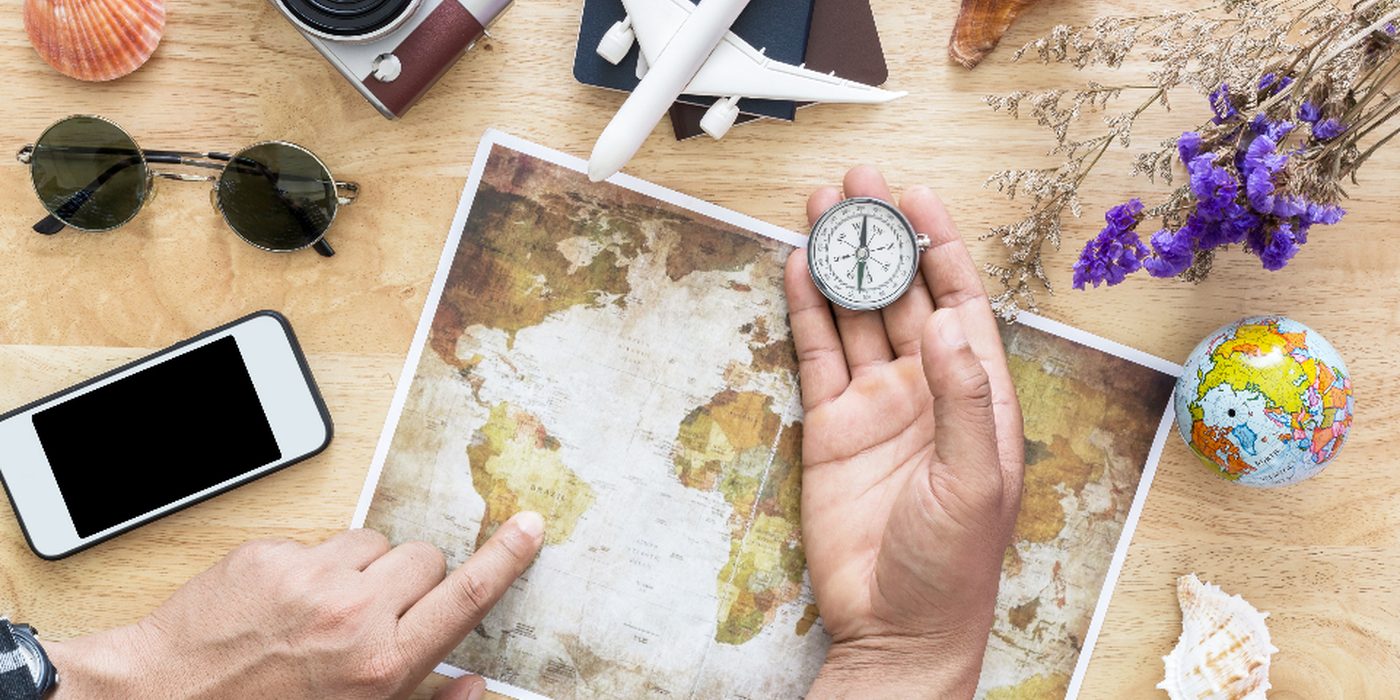 A flat-lay on a map of sunglasses, a phone, a pocket watch, a toy aeroplane and dried flowers.