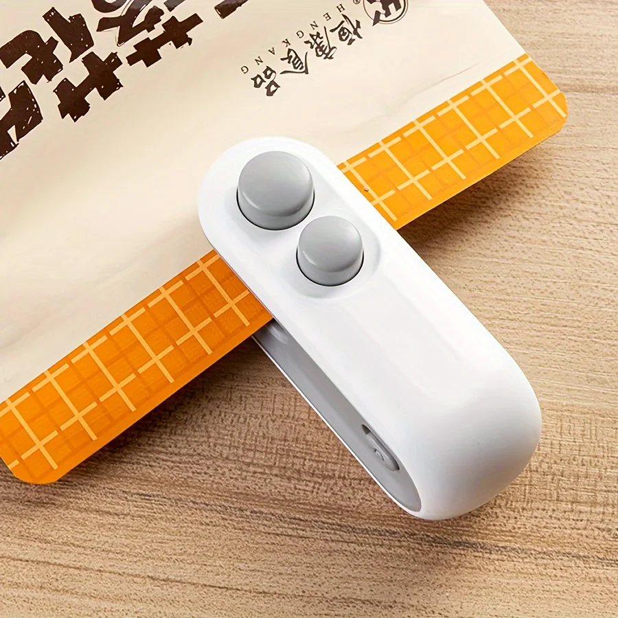 White mini bag sealer with two grey buttons clamped across the top edge of a printed snack bag on a wooden table