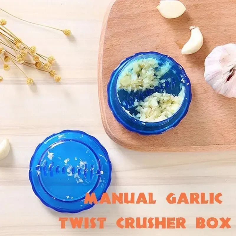 Blue garlic twist crusher on a wooden board holding minced garlic, lid alongside, with a garlic bulb and cloves nearby