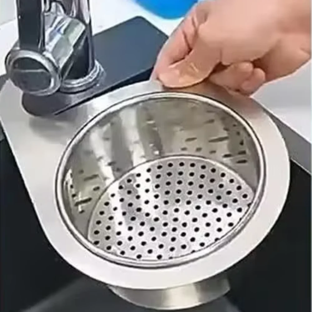 Hand lowering a stainless steel sink strainer basket into a kitchen sink drain opening beside the tap