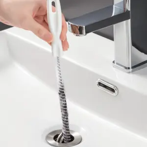 White-handled flexible drain cleaning brush being fed into a bathroom basin drain, hair caught in the spiral bristles