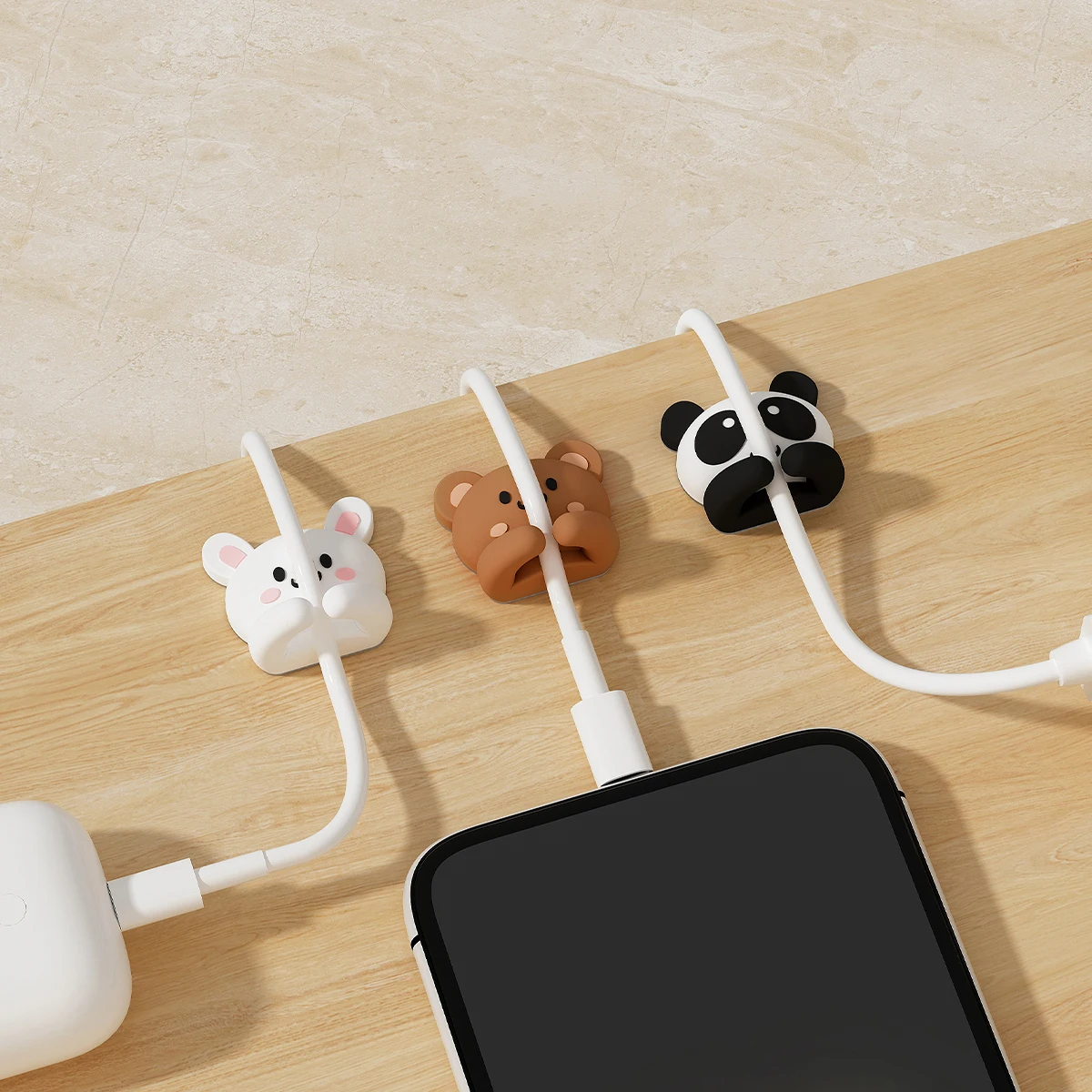 Overhead view of rabbit, bear and panda clips on a wooden desktop, guiding a white charging cable from a charger to a phone