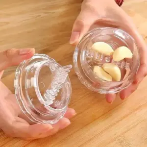 Hands holding the clear garlic twist crusher open, with peeled cloves in the base and a row of blade fins under the lid