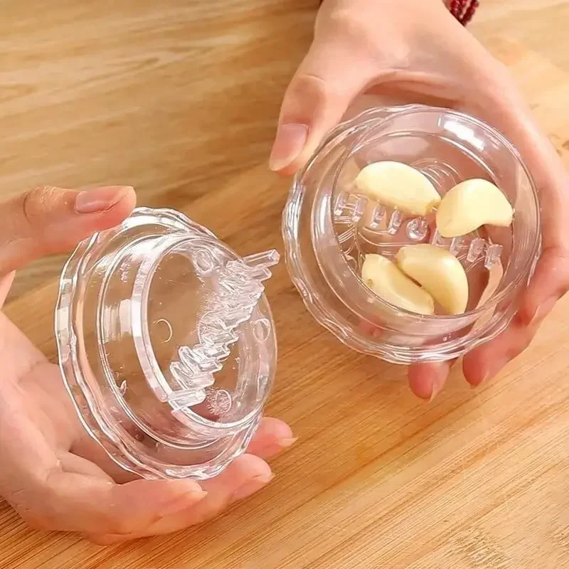 Hands holding the clear garlic twist crusher open, with peeled cloves in the base and a row of blade fins under the lid