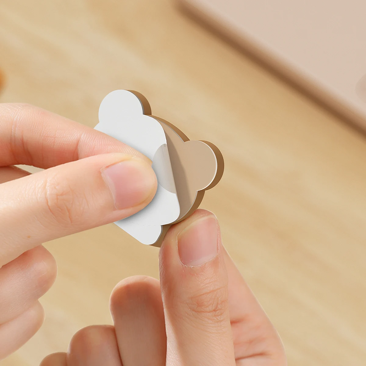Hand peeling the white backing paper off the adhesive pad on the back of a brown bear cable clip