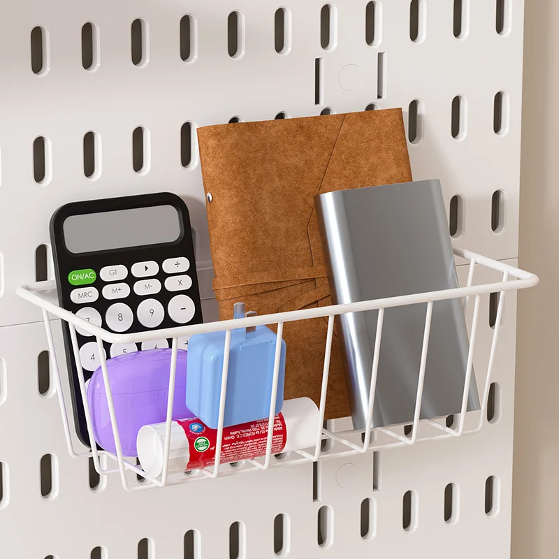 White wire pegboard basket holding a calculator, a notebook, a folder and glue sticks, clipped to a white slotted panel
