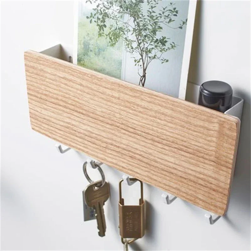 Close-up of the light wood key rack with white hooks holding a key and a brass padlock, a card and small pot in the tray