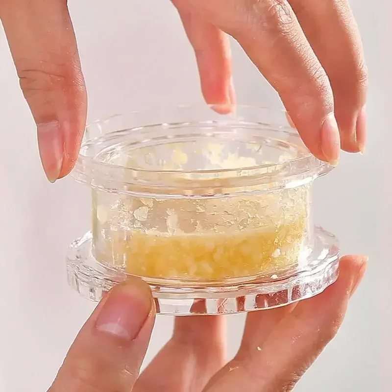 Hands twisting the lid of the clear garlic crusher, with minced garlic visible through the body of the pot