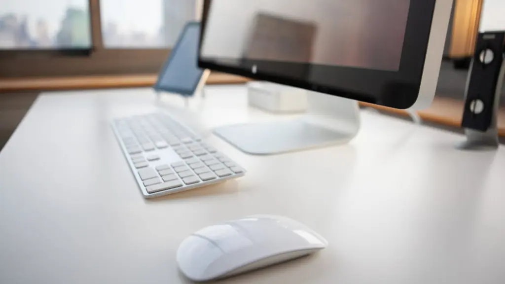 A clean white desk holding a monitor, a slim keyboard and a mouse, lit from a window behind.