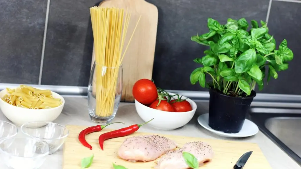 A kitchen counter with dried pasta, tomatoes, chillies and a basil plant beside a chopping board.