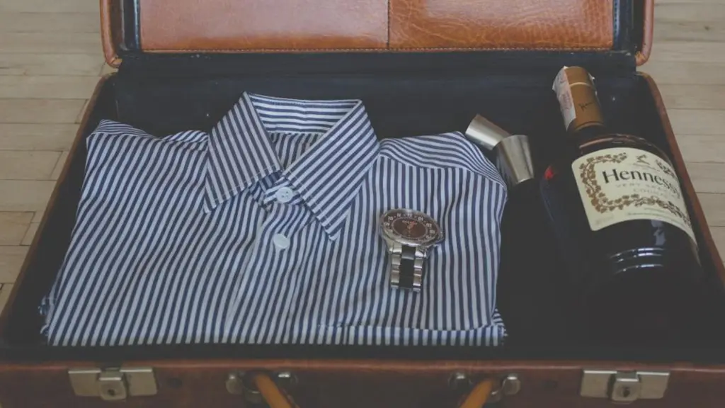 An open suitcase packed with a folded striped shirt, a bottle and a small leather case.